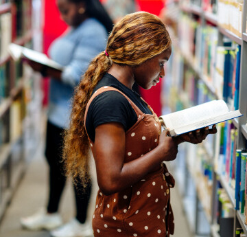 A student reading a book next to the library shelves