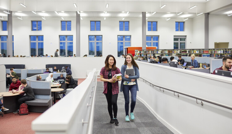 Two students carrying books while walking in Bay Library