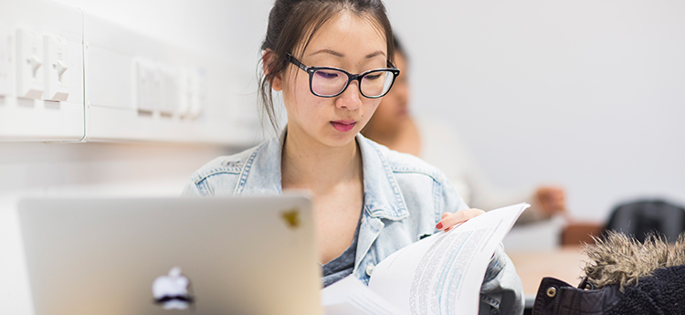 A female student wearing glasses sitting at laptop and reading a document