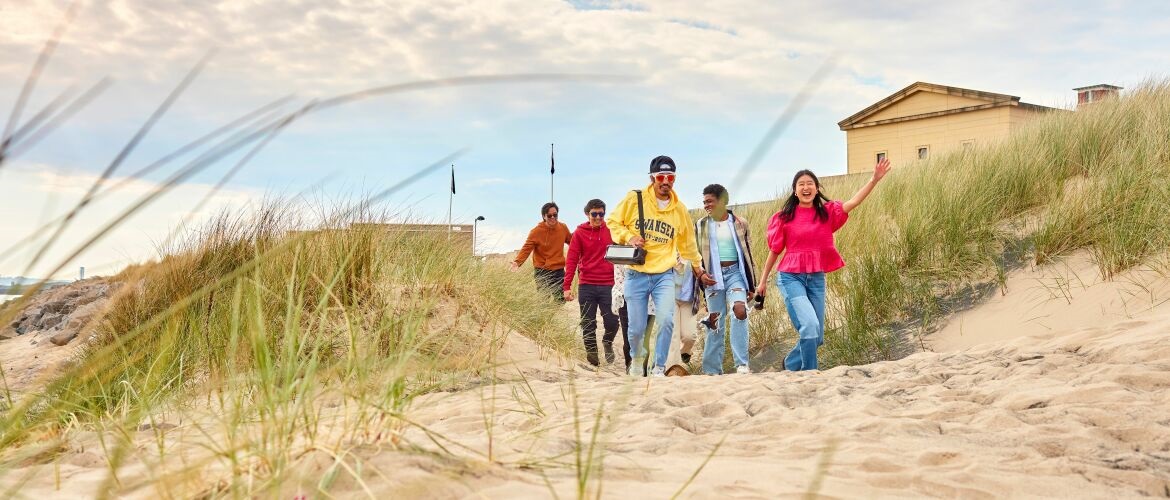 Students walking on the beach with the Great Hall in the background