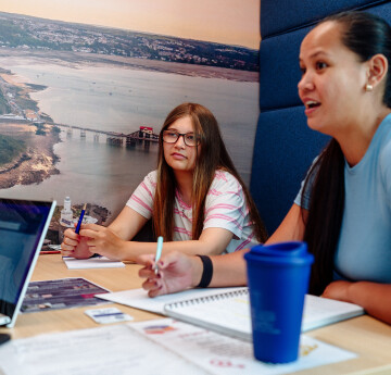 Myfyrwyr yn siarad mewn booth yn Adeilad Technoleg Ddigidol