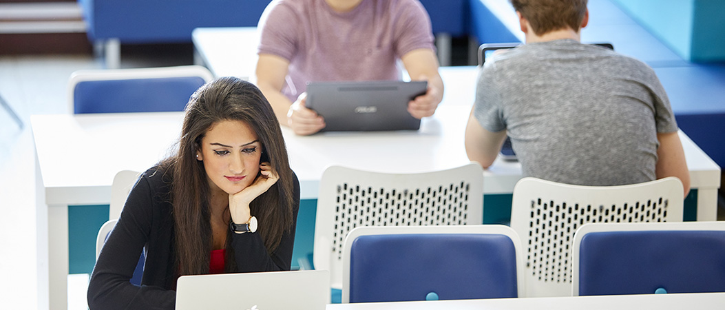 Students working on laptops at desks in a library