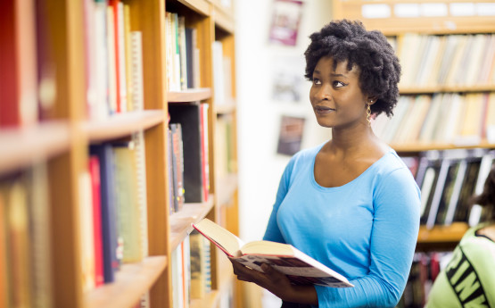 Student looking at book and bookshelves in Library