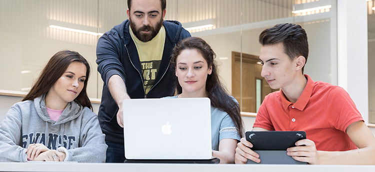 Students and a lecturer looking at a laptop. 