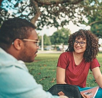 Two friends sitting on the lawn of a University, chatting and smiling