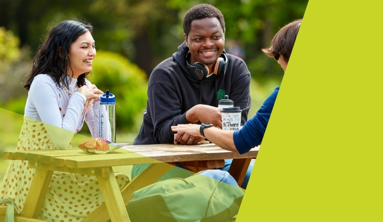 Three people sitting at a picnic table outdoors, engaged in conversation.